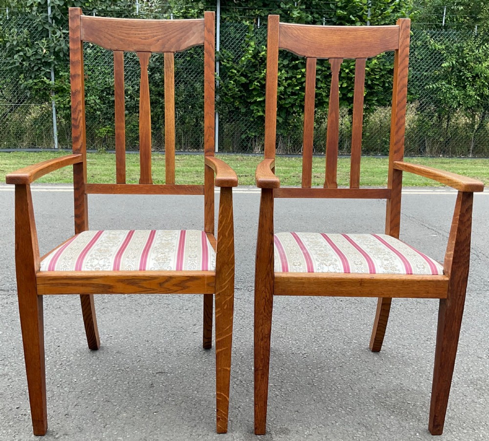 A pair of Edwardian oak highback armchairs featuring vertical back splats, tapered arm supports, and red and gold striped upholstered seats.