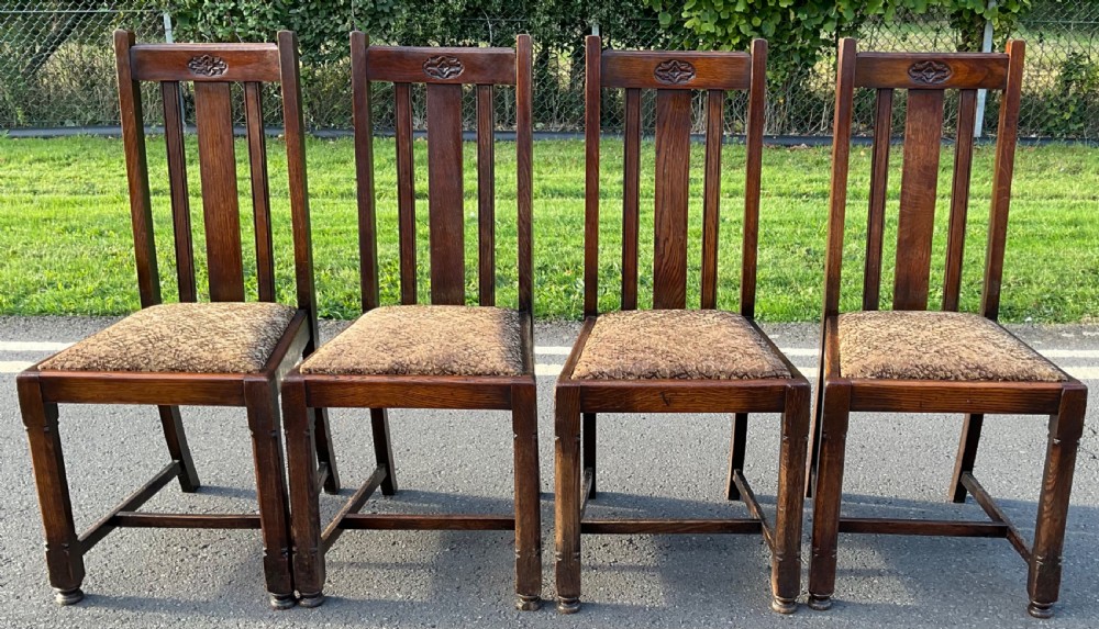 A set of four dark oak dining chairs featuring high slatted backrests with carved central details and patterned upholstered seats.