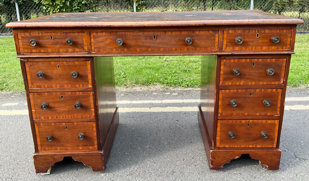 An antique Victorian mahogany kneehole writing desk featuring a dark leather top, multiple inset drawers with turned brass handles, crossbanded inlay, and bracket feet.