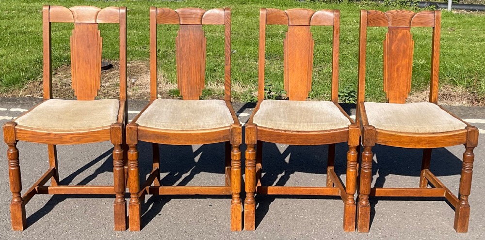 Set of four Art Deco oak dining chairs featuring geometric stepped splats, turned front legs, and neutral upholstered seats.