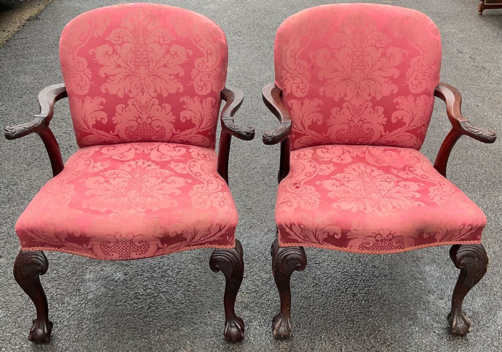 A pair of Georgian style open armchairs upholstered in patterned red damask fabric with carved mahogany cabriole legs ending in ball and claw feet.