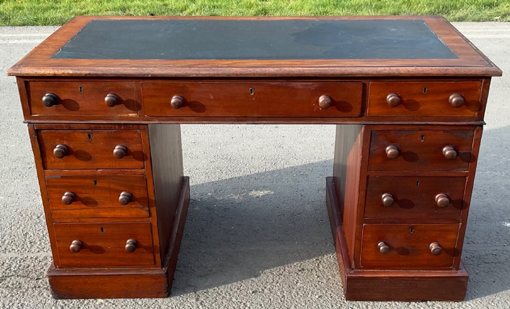 A Victorian mahogany pedestal writing desk featuring a dark writing insert on top and nine drawers with turned wooden handles.