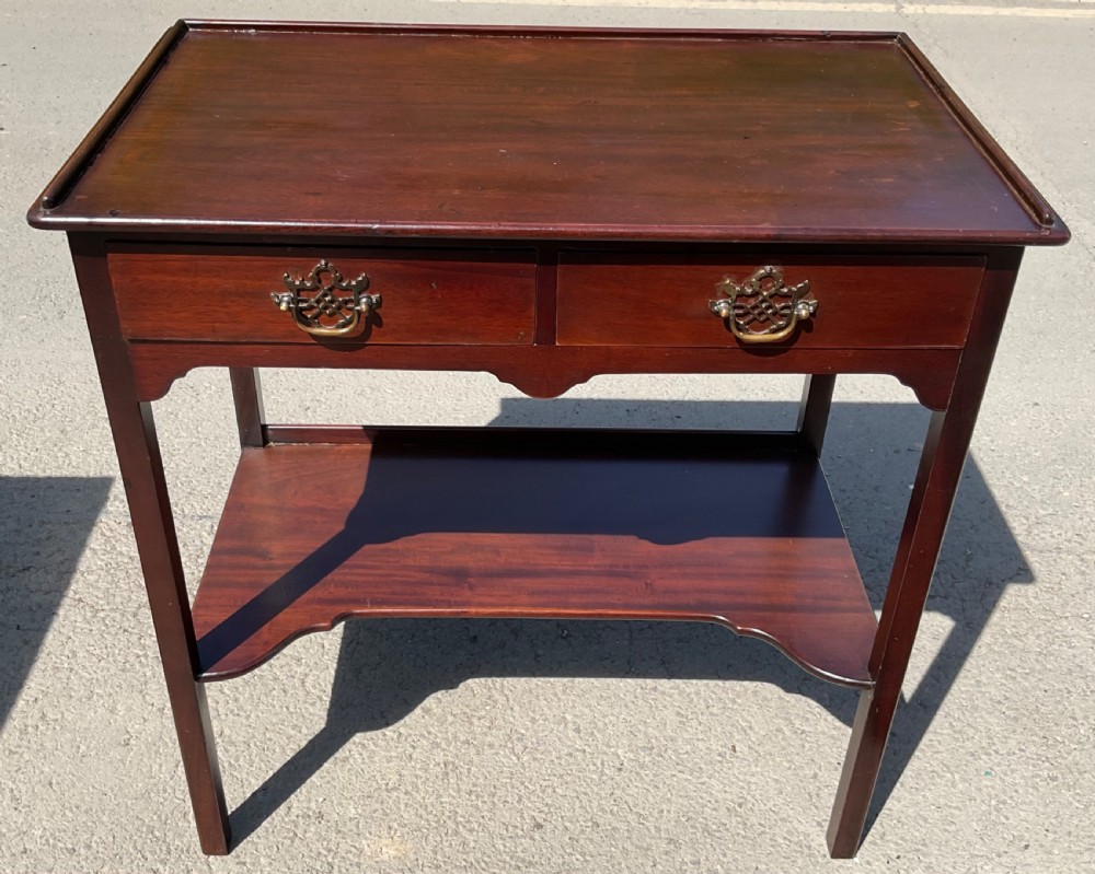 An Edwardian dark mahogany two-tier side table featuring two drawers with decorative brass handles, straight legs, and a lower shelf.