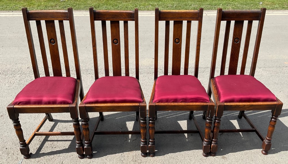Set of four dark oak dining chairs with vertical slat backs, central carved roundels, turned front legs, and red upholstered seats.