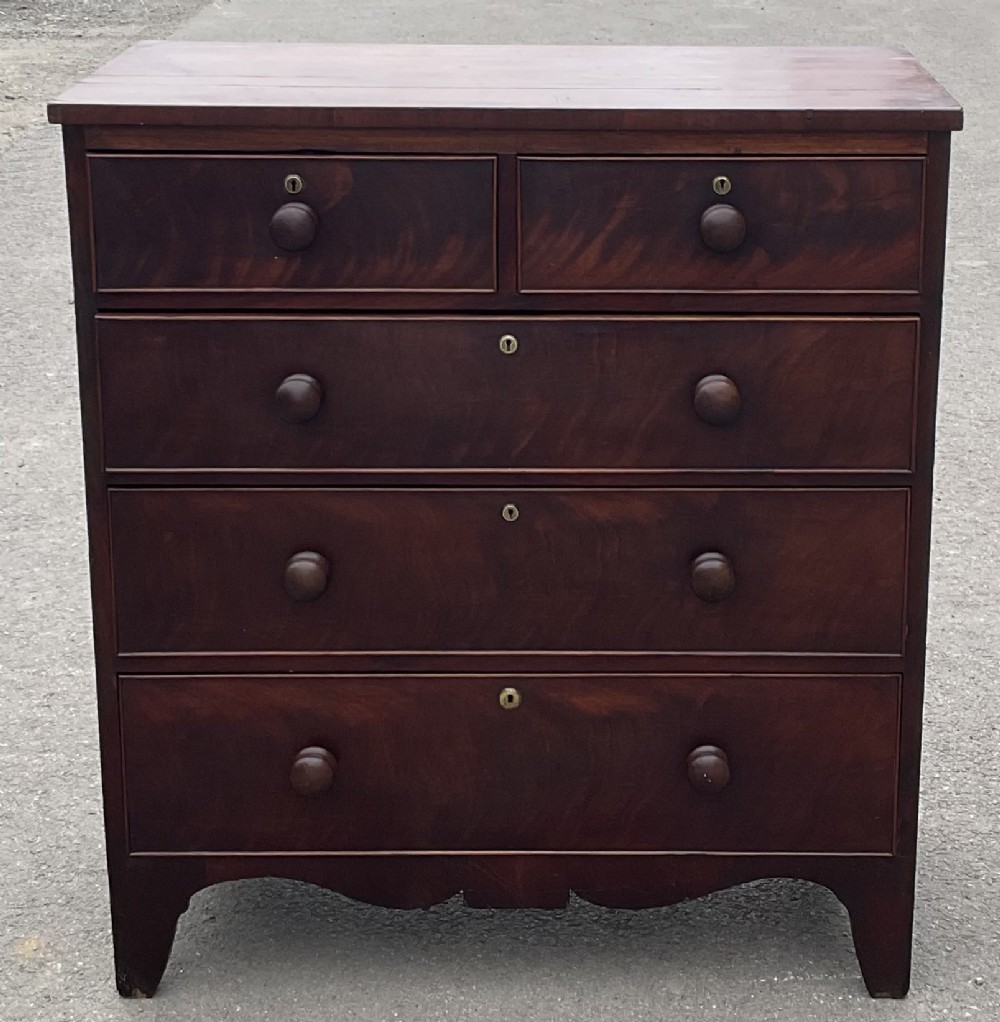 A Georgian dark mahogany chest of drawers featuring a two-over-three drawer layout, turned wooden handles, brass keyhole surrounds, and a bracket-style base.