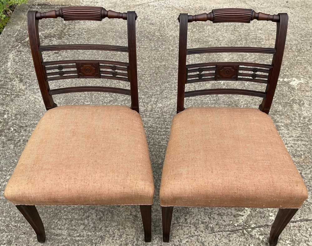 A pair of Georgian mahogany dining chairs with reeded frames, carved back rails, and beige fabric upholstered seats. View V