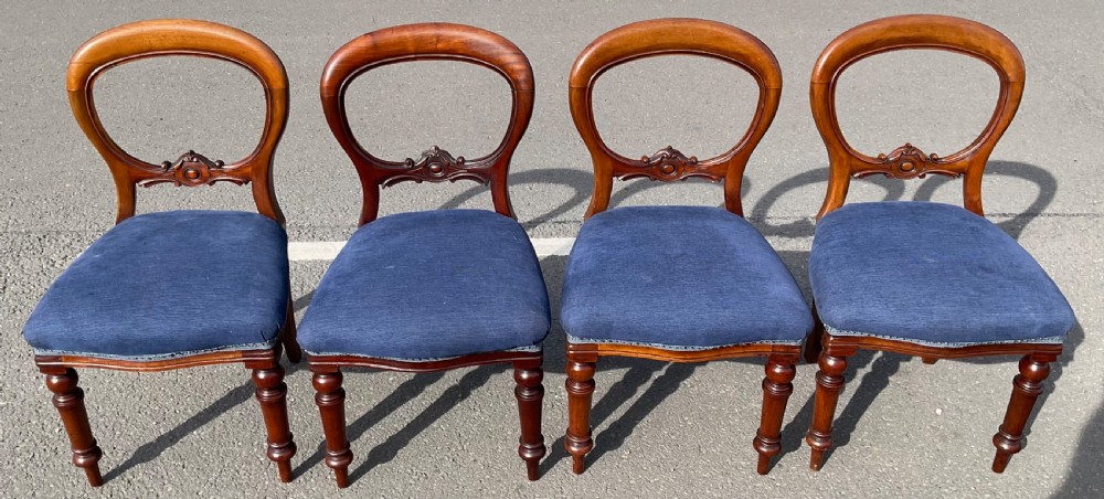 A set of four Victorian mahogany dining chairs featuring rounded balloon backs, carved horizontal mid-rails, blue fabric seats, and turned front legs.