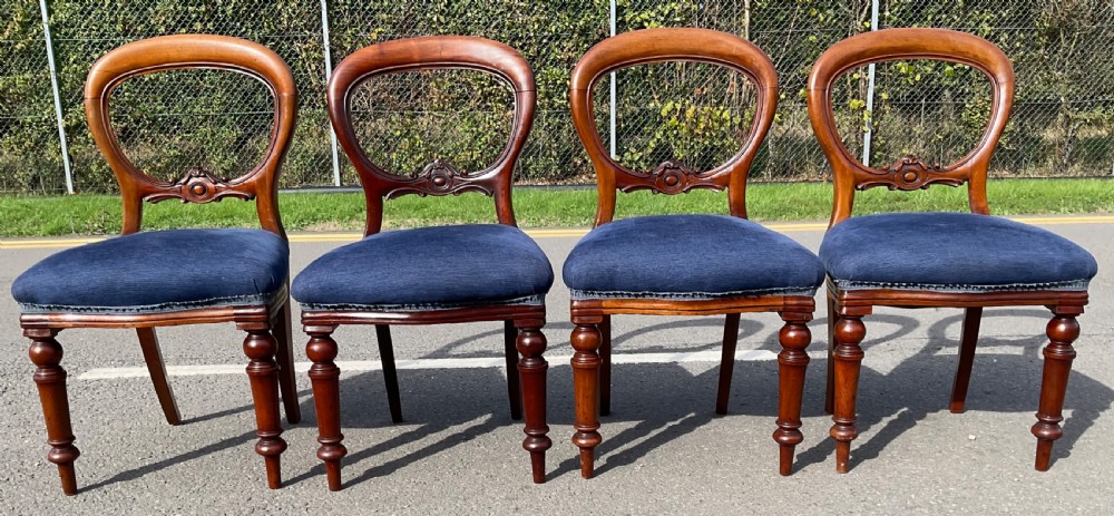 A set of four Victorian mahogany dining chairs featuring rounded balloon backs, carved horizontal mid-rails, blue fabric seats, and turned front legs. View II