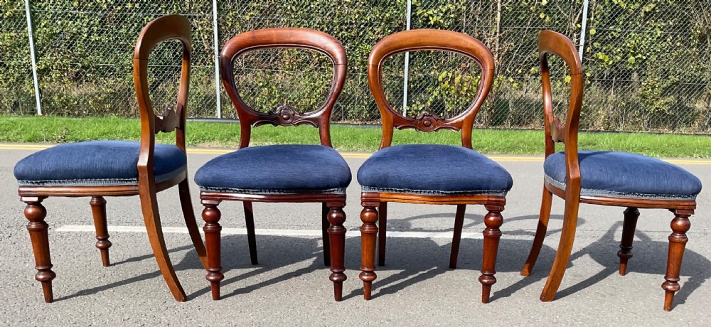 A set of four Victorian mahogany dining chairs featuring rounded balloon backs, carved horizontal mid-rails, blue fabric seats, and turned front legs. View IV