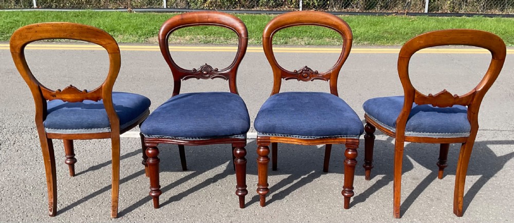 A set of four Victorian mahogany dining chairs featuring rounded balloon backs, carved horizontal mid-rails, blue fabric seats, and turned front legs. View V