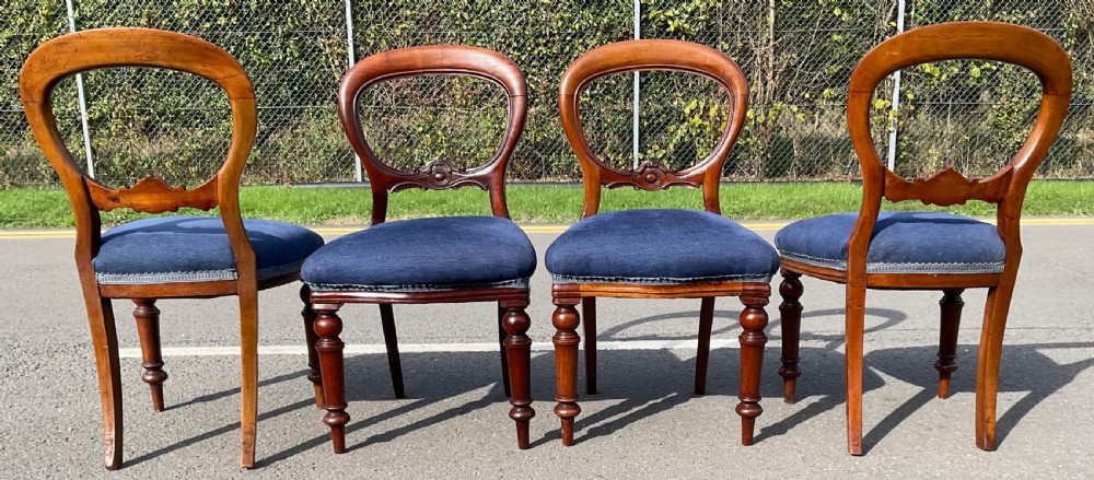 A set of four Victorian mahogany dining chairs featuring rounded balloon backs, carved horizontal mid-rails, blue fabric seats, and turned front legs. View VI