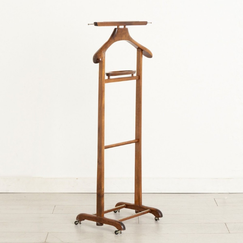 An Edwardian beech wood valet stand featuring a contoured coat hanger, small accessories dish, trouser bar, and a four-footed base on castors.
