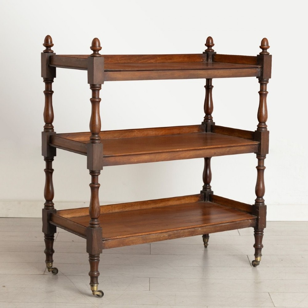 A three-tier Victorian mahogany buffet featuring turned spindle supports, urn finials, three open shelves, and brass castors.
