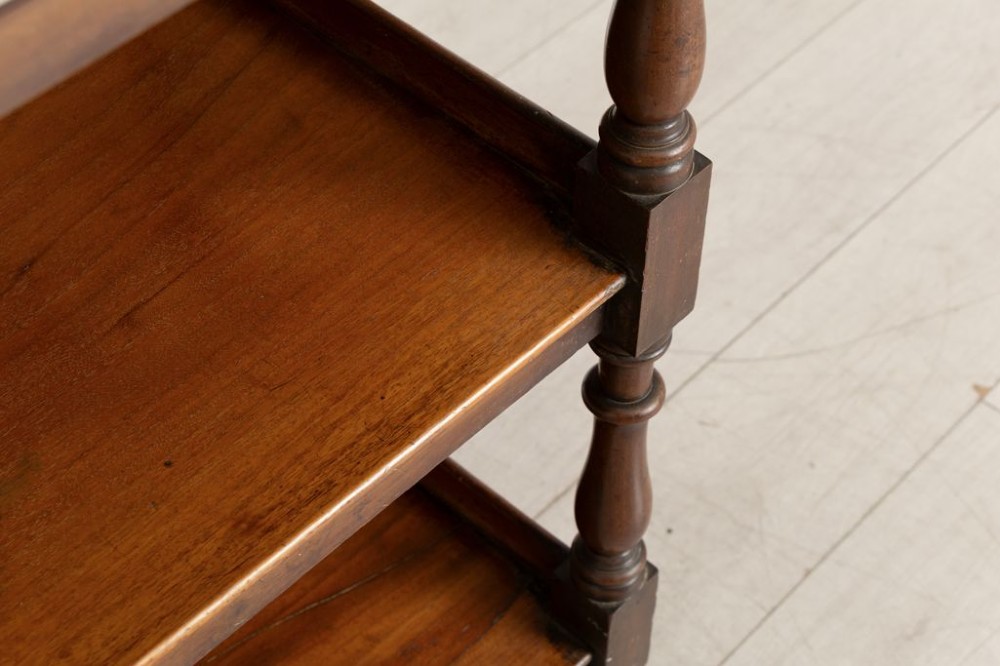 A three-tier Victorian mahogany buffet featuring turned spindle supports, urn finials, three open shelves, and brass castors. View III