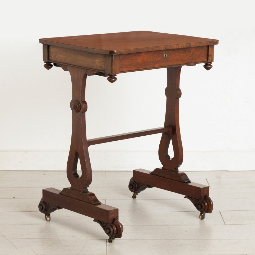 A Victorian rosewood side table featuring a single frieze drawer, shaped trestle supports, a central stretcher, and carved scroll feet fitted with brass castors.