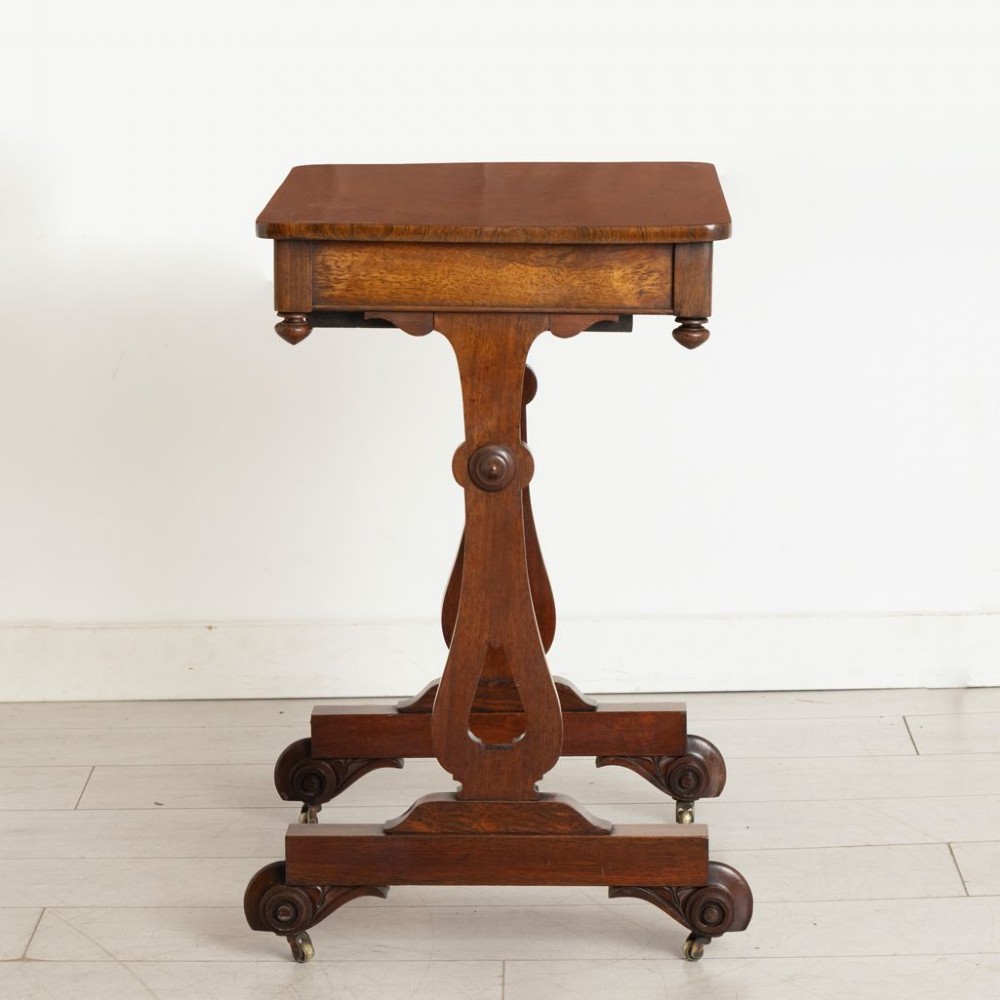 A Victorian rosewood side table featuring a single frieze drawer, shaped trestle supports, a central stretcher, and carved scroll feet fitted with brass castors. View III