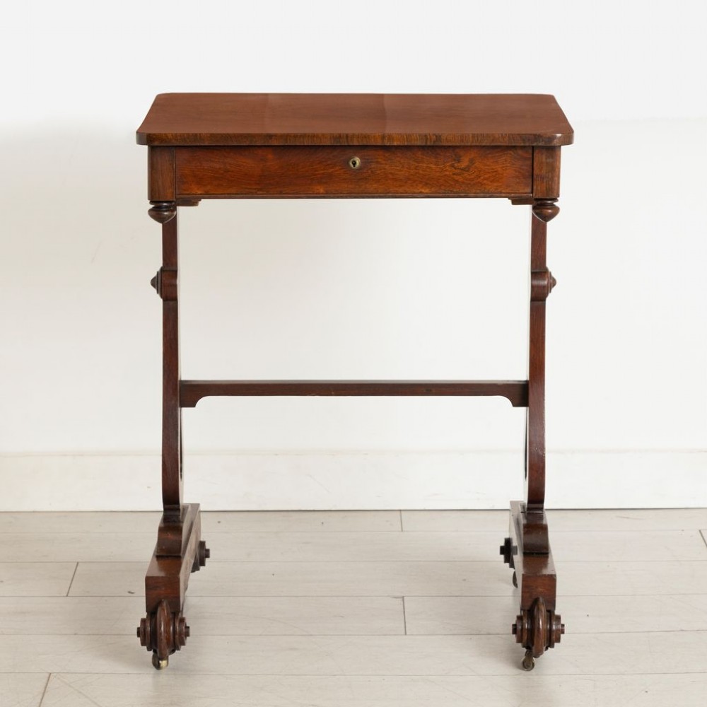 A Victorian rosewood side table featuring a single frieze drawer, shaped trestle supports, a central stretcher, and carved scroll feet fitted with brass castors. View IV