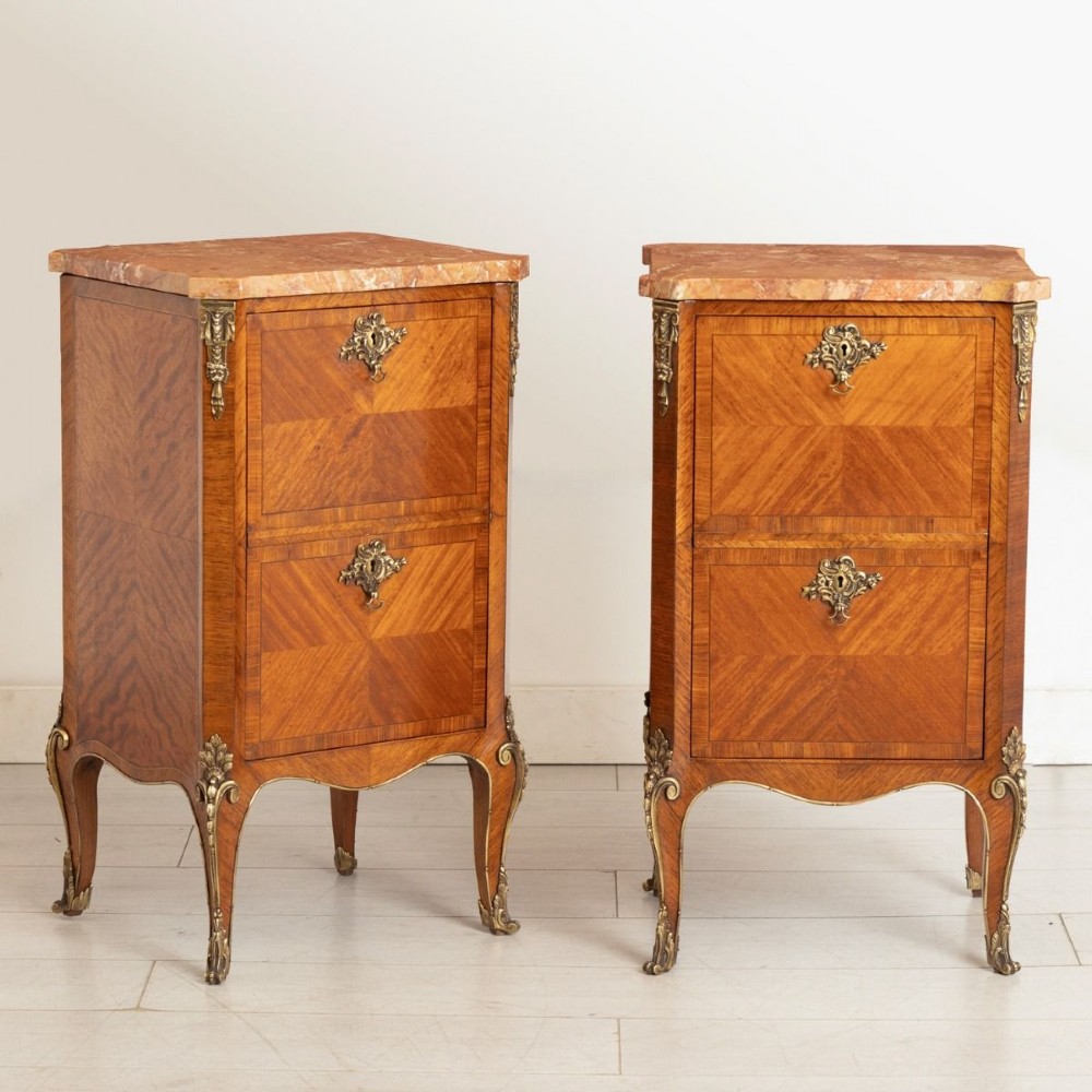 A matching pair of French 19th-century walnut and kingwood bedside cabinets featuring pink marble tops, parquetry drawer fronts, cabriole legs, and ornate brass mounts.