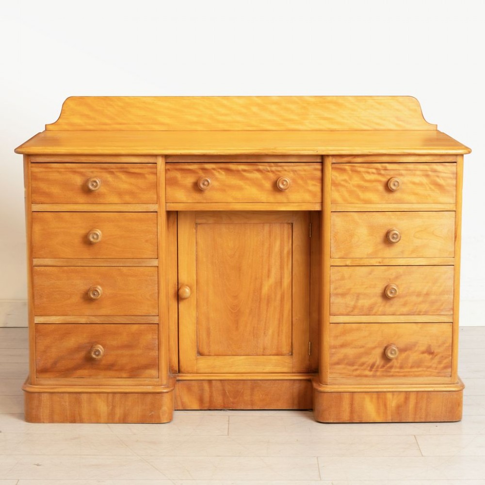 A Victorian satin birch kneehole desk featuring a low gallery top, central cupboard door, surrounding drawers, and turned wooden handles.