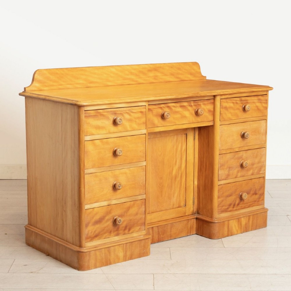 A Victorian satin birch kneehole desk featuring a low gallery top, central cupboard door, surrounding drawers, and turned wooden handles. View II