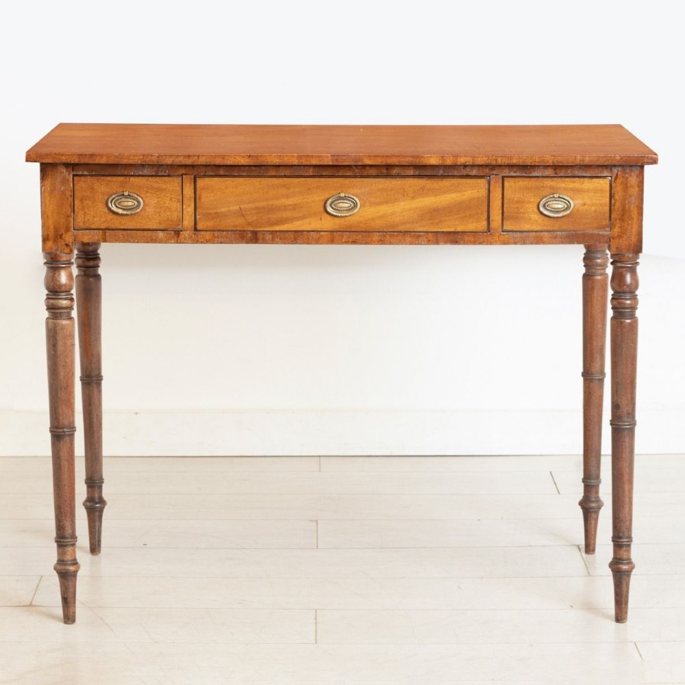 A 19th-century mahogany writing table featuring three frieze drawers with oval brass handles and four slender turned legs.
