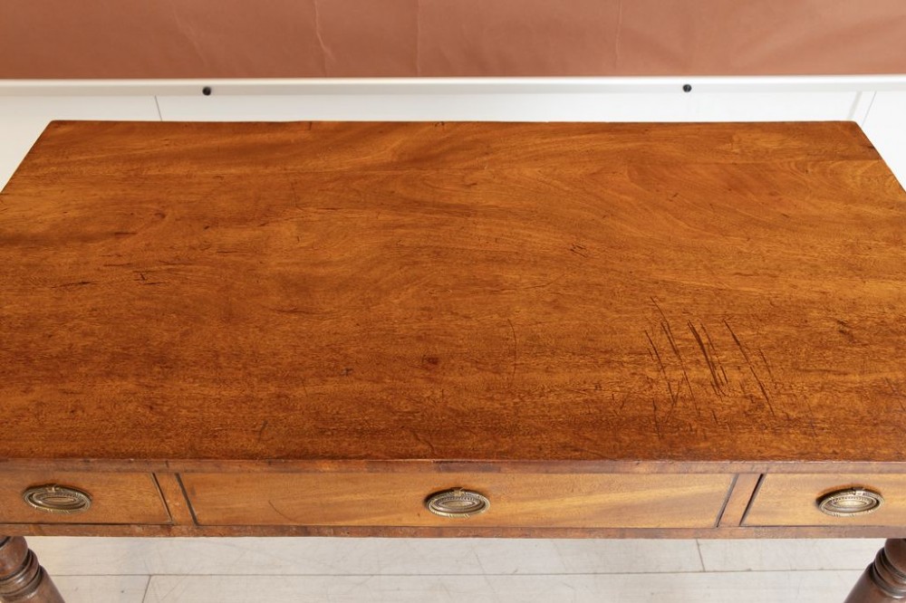 A 19th-century mahogany writing table featuring three frieze drawers with oval brass handles and four slender turned legs. View IV