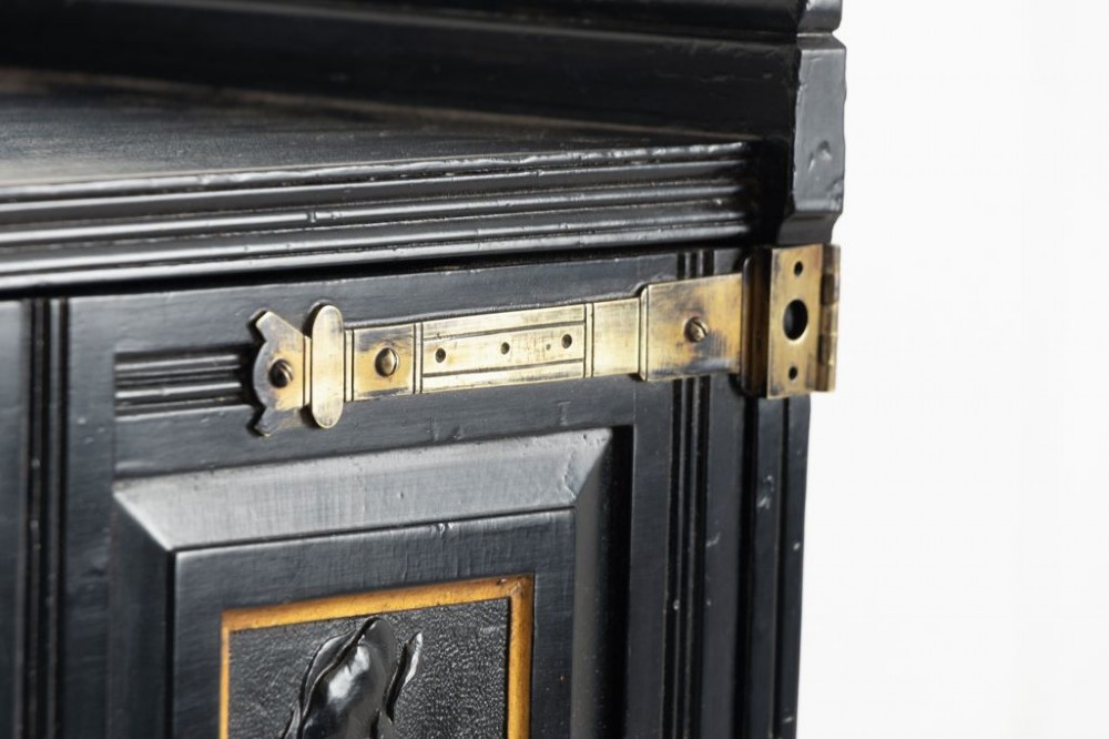 A late 19th-century Aesthetic Movement ebonised music cabinet featuring carved botanical upper doors with brass corner mounts and open vertical sheet music slots below. View III