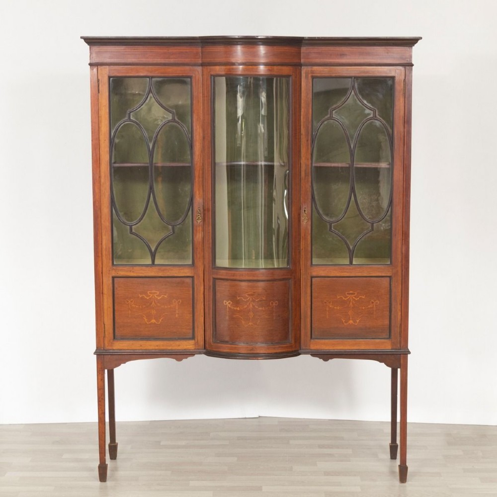 An Edwardian mahogany china cabinet featuring three glazed doors with oval astragal moulding, inlaid lower panels, and slender square legs.