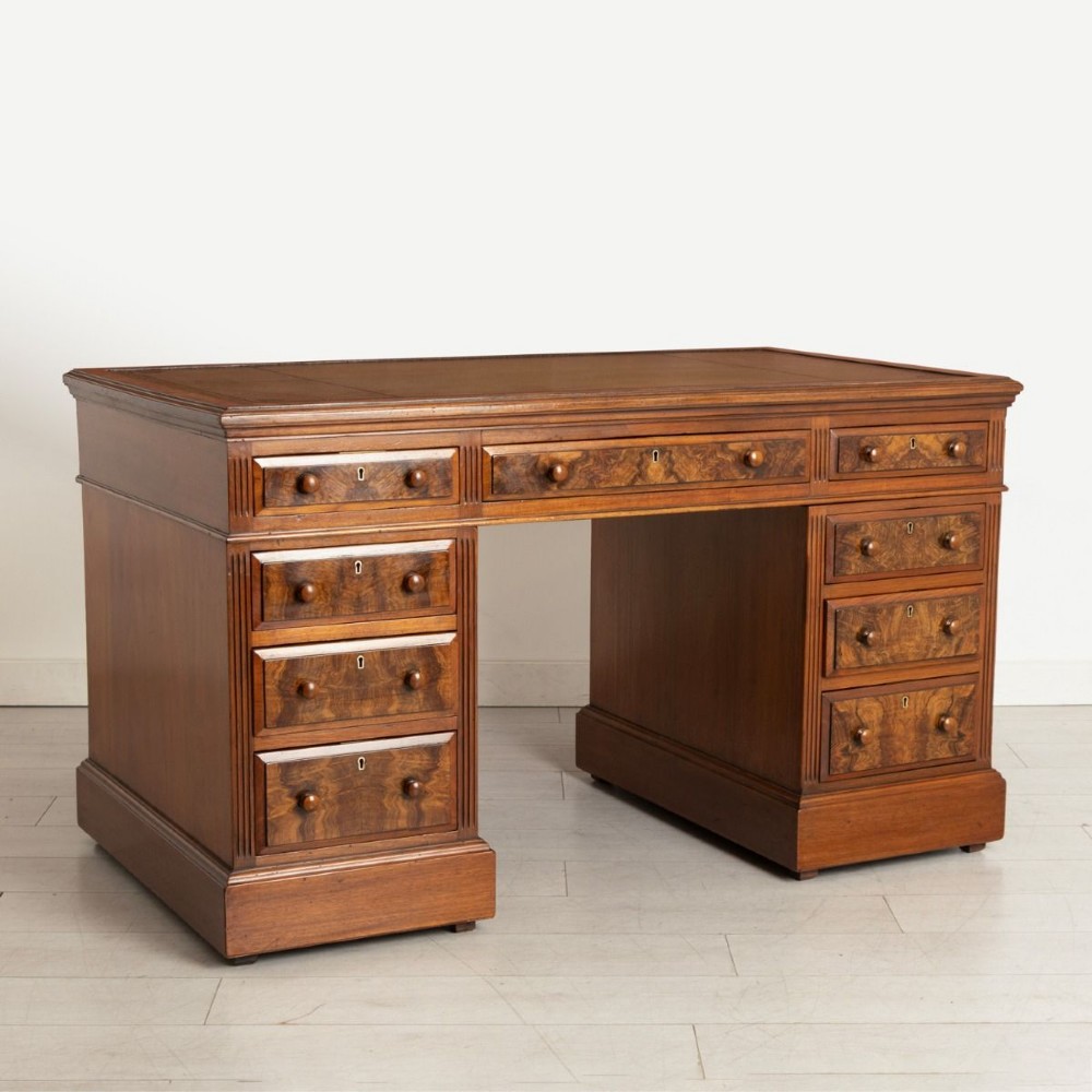 A nineteenth-century Victorian walnut pedestal desk featuring decorative burr walnut drawer fronts, turned wooden handles, a green leather writing surface, and a sturdy plinth base.