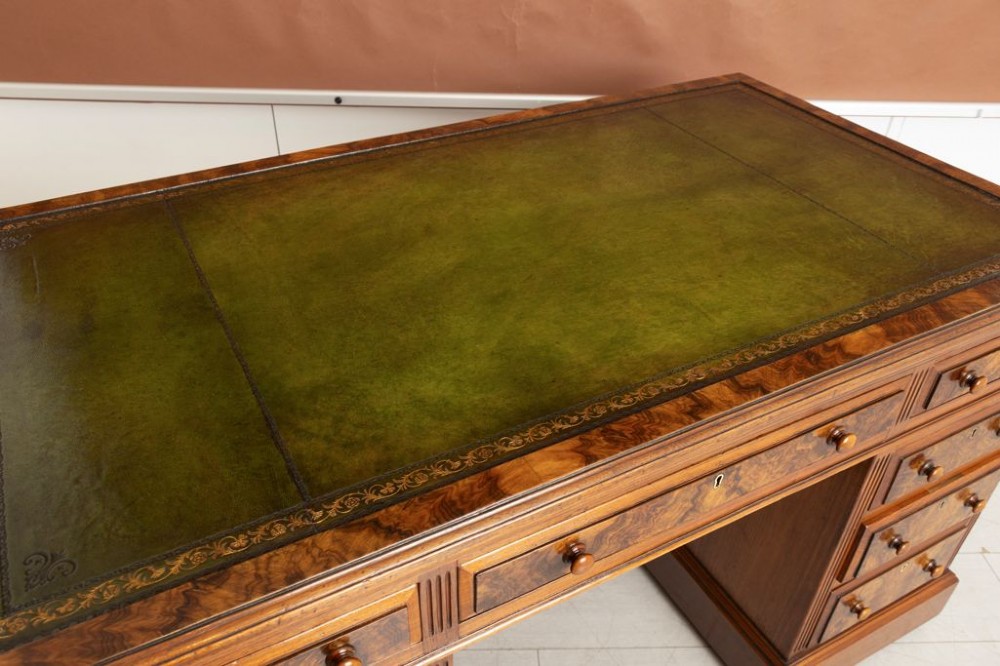 A nineteenth-century Victorian walnut pedestal desk featuring decorative burr walnut drawer fronts, turned wooden handles, a green leather writing surface, and a sturdy plinth base. View IV