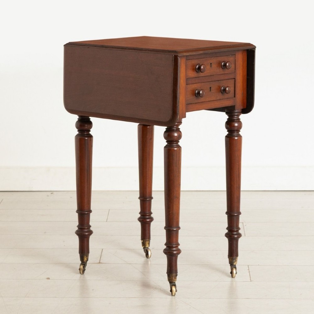 A Victorian mahogany drop-leaf side table featuring two front drawers with turned wooden knobs, ring-turned legs, and brass castors.