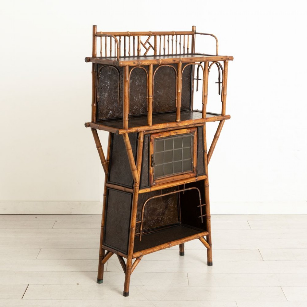 An antique Victorian bamboo display cabinet featuring an upper gallery shelf, open compartments with dark embossed panels, and a central leaded glass door. View II