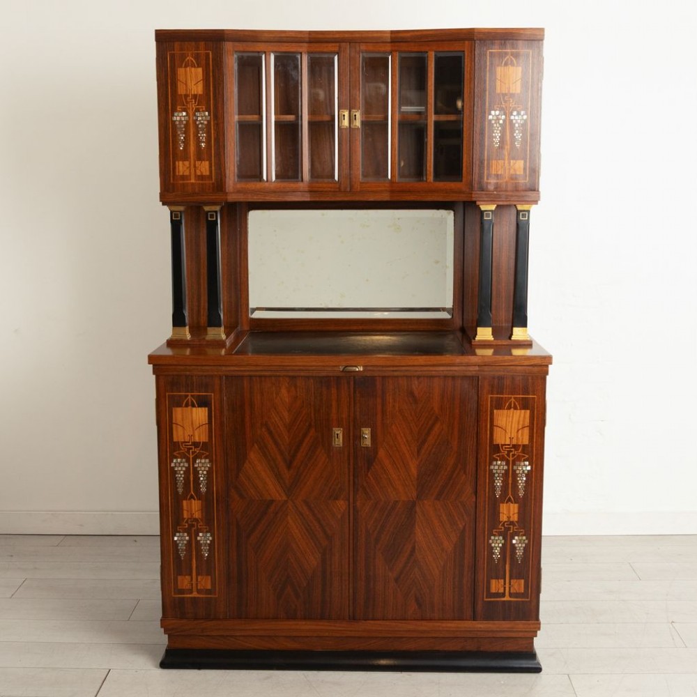An antique Viennese Secessionist walnut display cabinet featuring geometric marquetry inlays, ebonised column supports, upper glazed doors, a central mirrored niche, and a lower two-door cupboard.