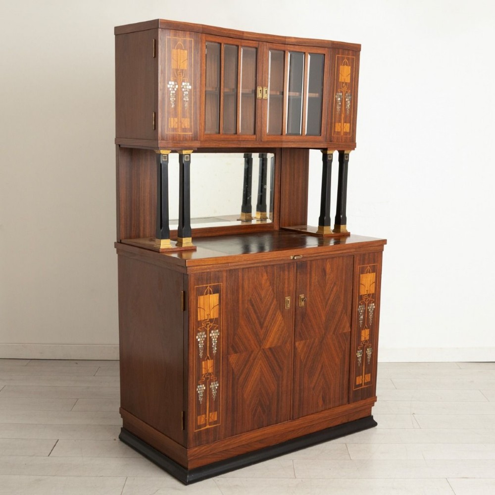 An antique Viennese Secessionist walnut display cabinet featuring geometric marquetry inlays, ebonised column supports, upper glazed doors, a central mirrored niche, and a lower two-door cupboard. View III