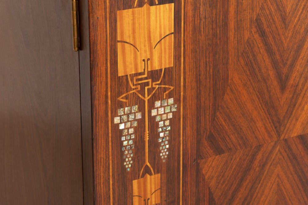 An antique Viennese Secessionist walnut display cabinet featuring geometric marquetry inlays, ebonised column supports, upper glazed doors, a central mirrored niche, and a lower two-door cupboard. View V