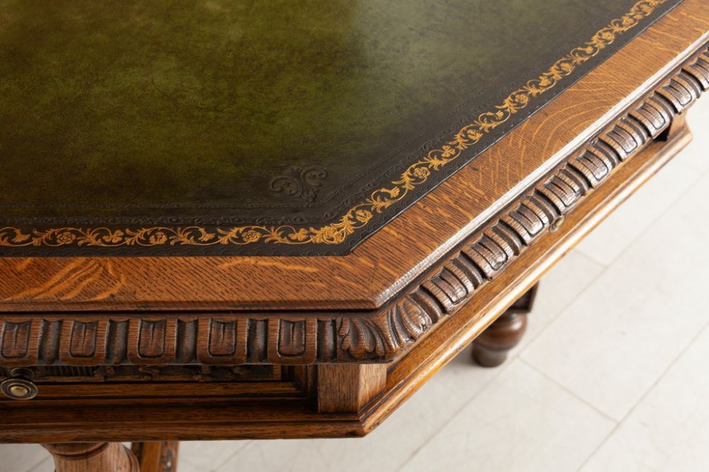 An antique Victorian octagonal oak library table with a green leather inset writing top, relief-carved frieze drawers, turned legs, and a carved X-stretcher. View III