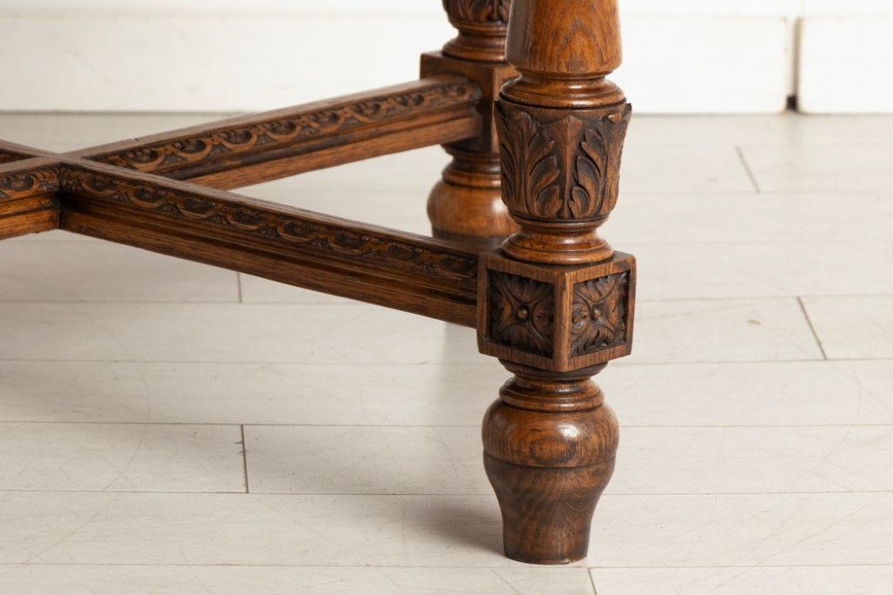 An antique Victorian octagonal oak library table with a green leather inset writing top, relief-carved frieze drawers, turned legs, and a carved X-stretcher. View VI