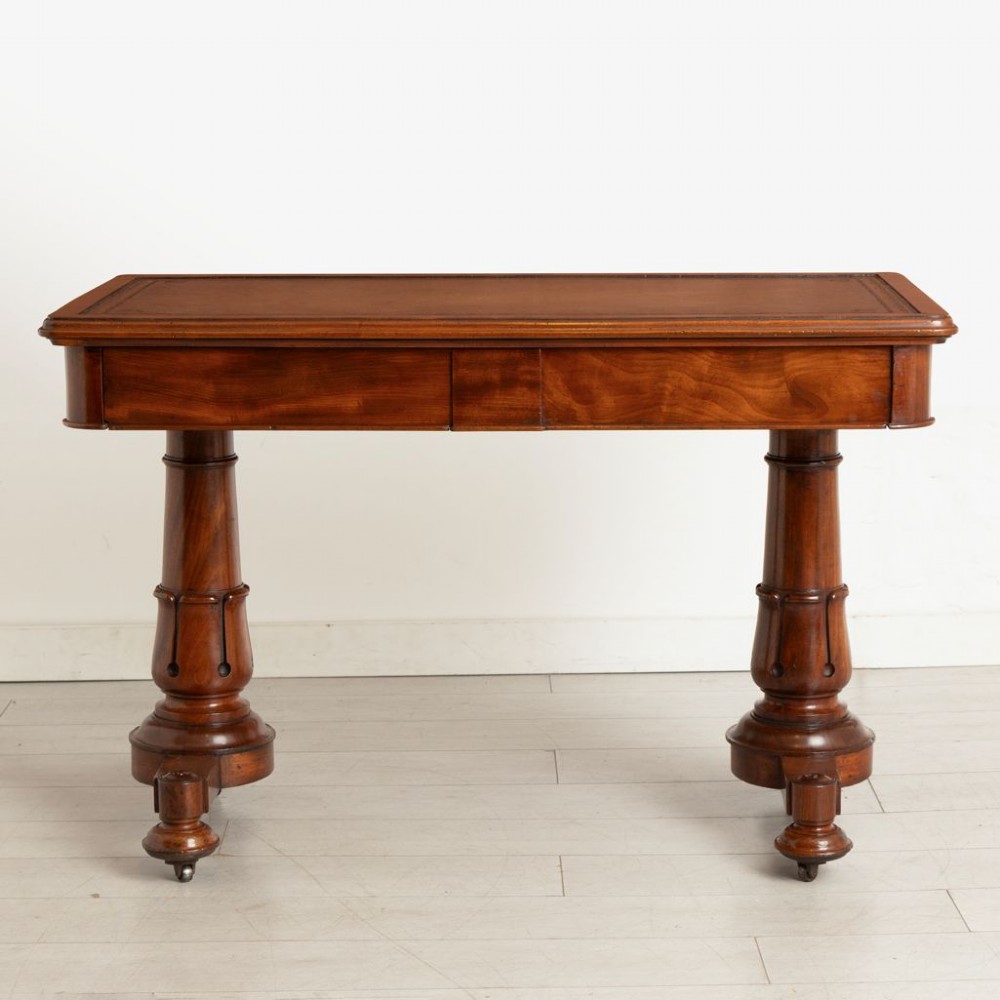 A Regency mahogany library table with a rectangular tan leather writing top, frieze drawers, turned column supports, and brass castors.