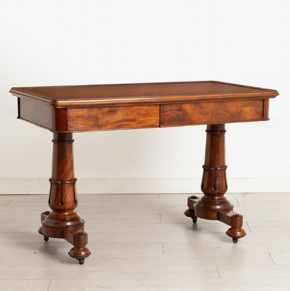 A Regency mahogany library table with a rectangular tan leather writing top, frieze drawers, turned column supports, and brass castors. View II