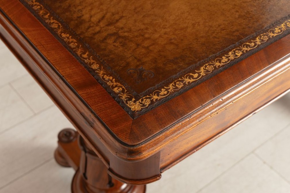 A Regency mahogany library table with a rectangular tan leather writing top, frieze drawers, turned column supports, and brass castors. View IV
