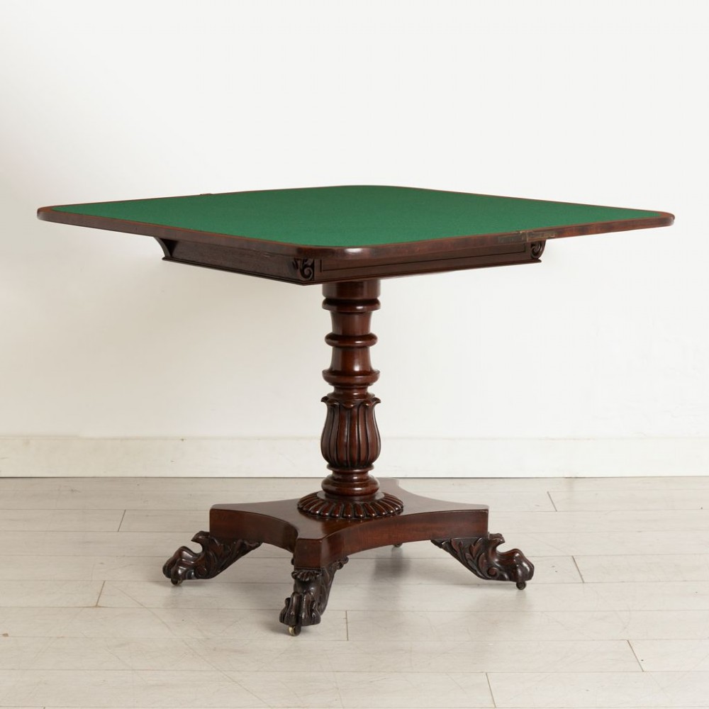 A Late Georgian mahogany fold-over card table featuring a turned carved pedestal stem and a quadform base with carved scroll feet on castors. View III