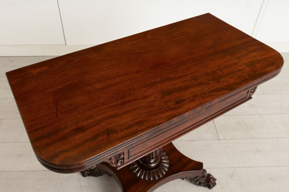 A Late Georgian mahogany fold-over card table featuring a turned carved pedestal stem and a quadform base with carved scroll feet on castors. View IV