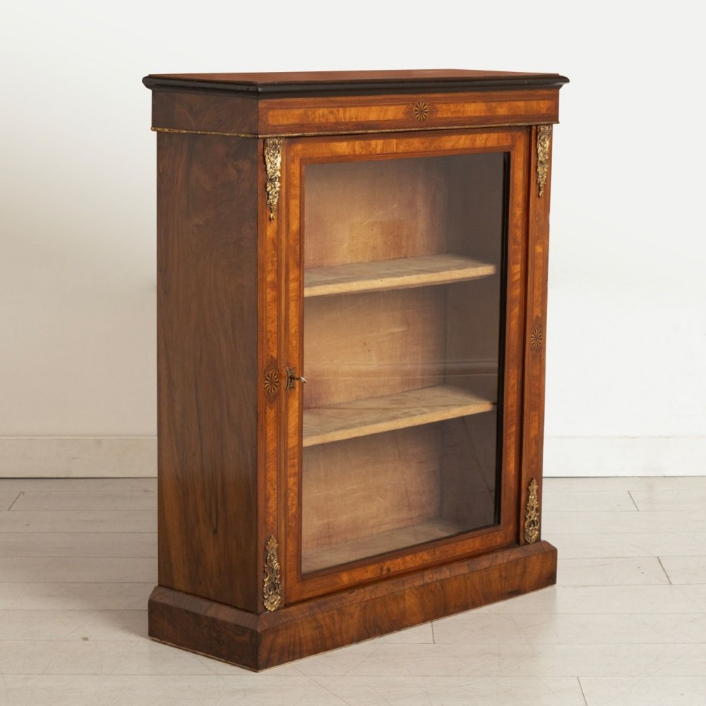 A Victorian burr walnut pier cabinet featuring a single glazed door, ebony and rosewood inlay detailing, interior wooden shelves, and gilt brass ormolu corner mounts. View II