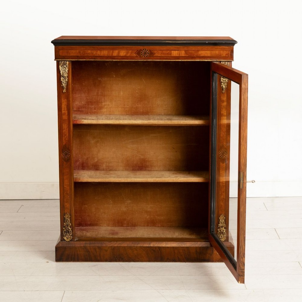 A Victorian burr walnut pier cabinet featuring a single glazed door, ebony and rosewood inlay detailing, interior wooden shelves, and gilt brass ormolu corner mounts. View III