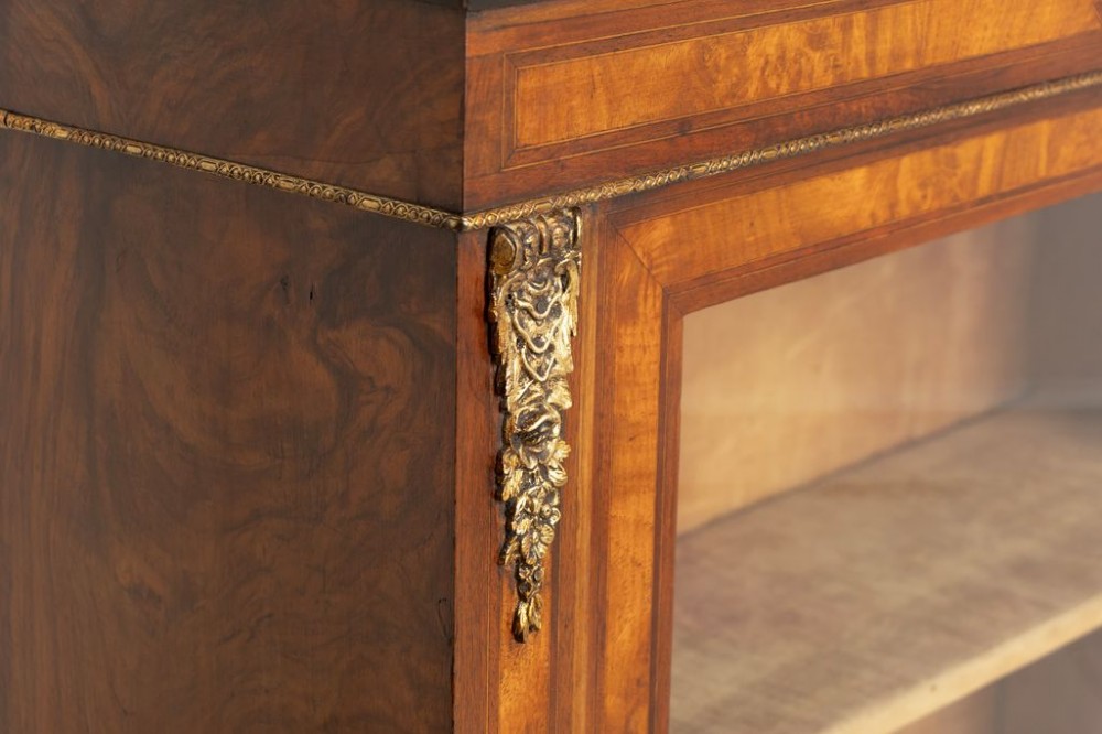 A Victorian burr walnut pier cabinet featuring a single glazed door, ebony and rosewood inlay detailing, interior wooden shelves, and gilt brass ormolu corner mounts. View IV