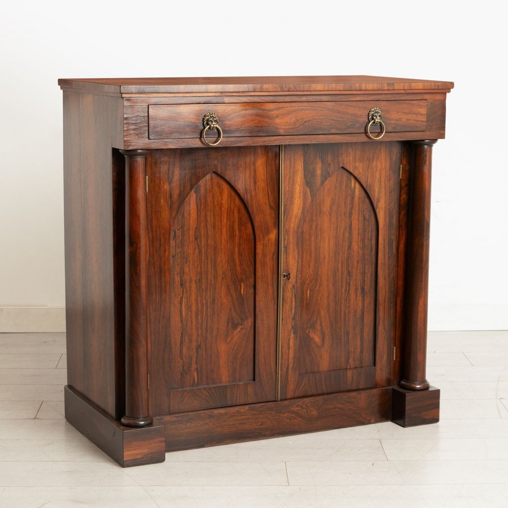 A Regency rosewood chiffonier with a long top drawer featuring brass lion-mask handles above twin doors with Gothic arched panels flanked by turned columns.