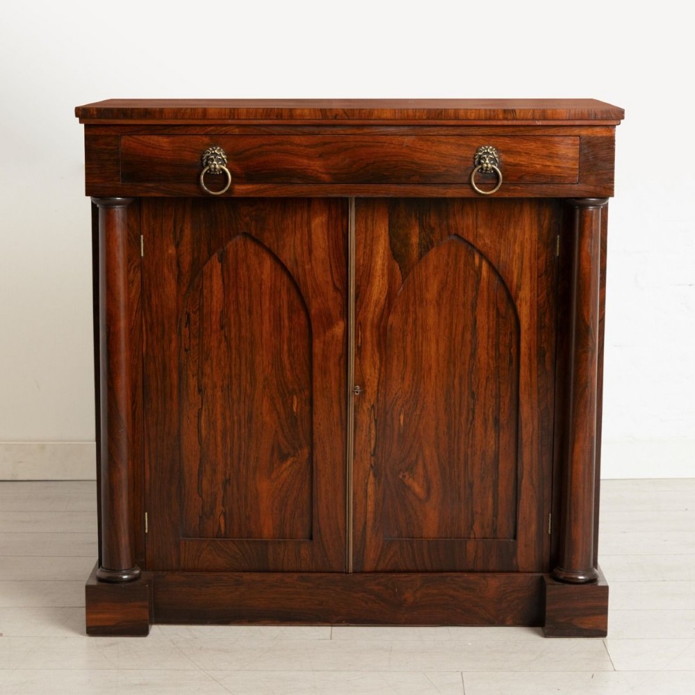 A Regency rosewood chiffonier with a long top drawer featuring brass lion-mask handles above twin doors with Gothic arched panels flanked by turned columns. View II