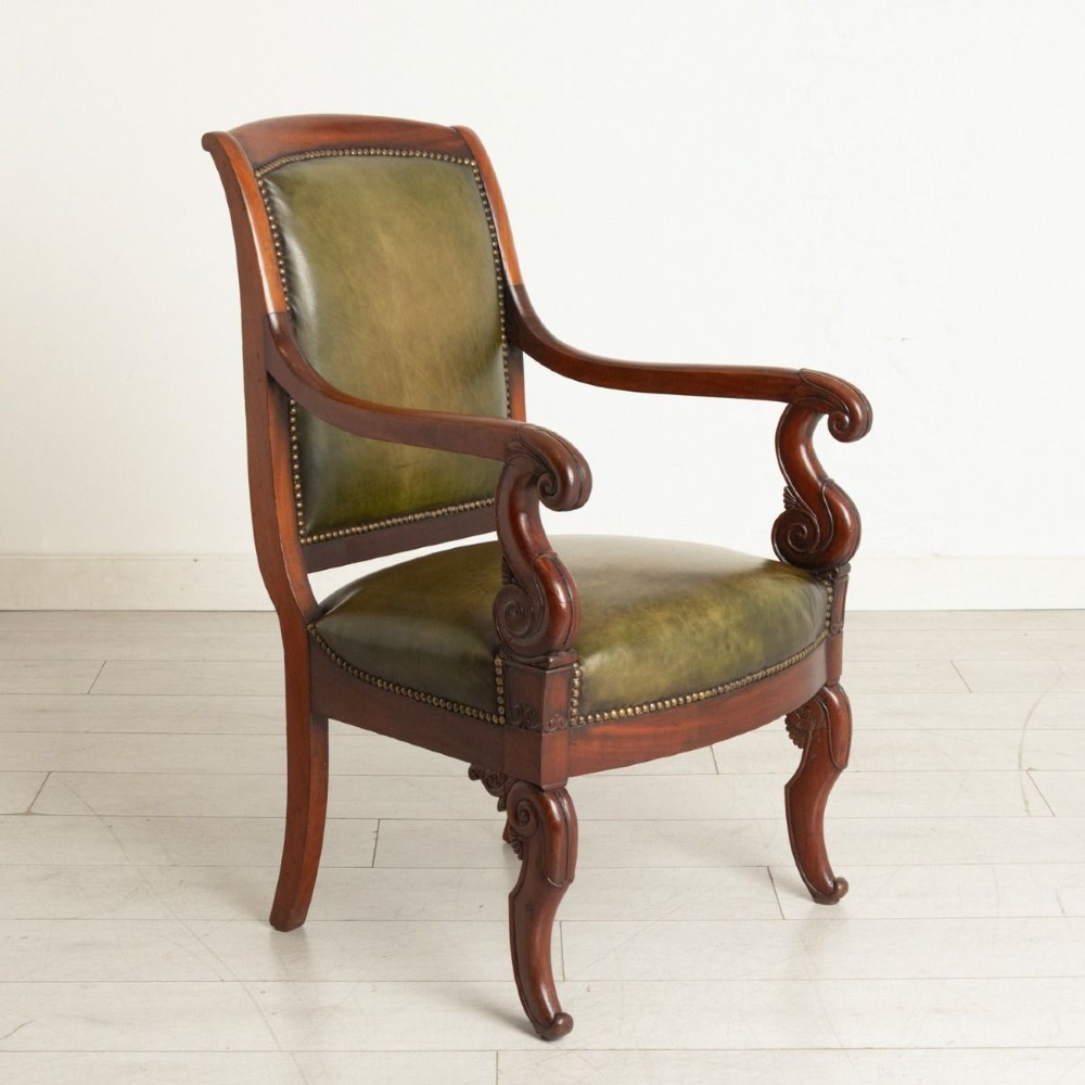 A Regency mahogany library chair featuring olive green leather upholstery with brass stud trim, carved scroll arms, and shaped legs.