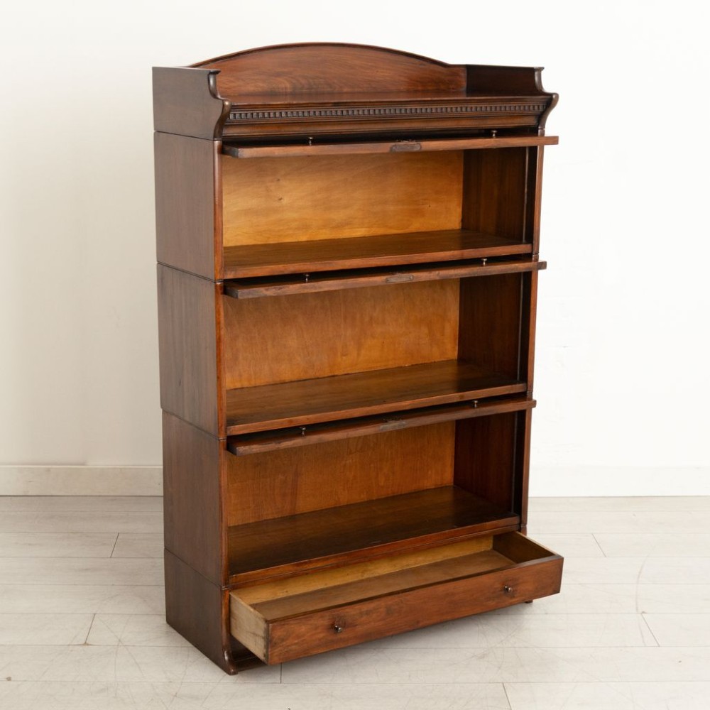 An Edwardian oak three-tier sectional bookcase featuring up-and-over glazed doors, an arched pediment top, and a base drawer with wooden knobs. View II