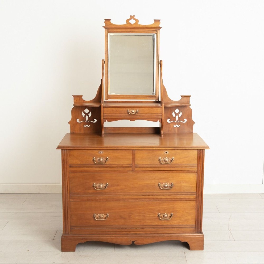 An Arts and Crafts walnut dressing chest featuring two short over two long drawers, a mirror superstructure, and decorative pierced cut-outs.